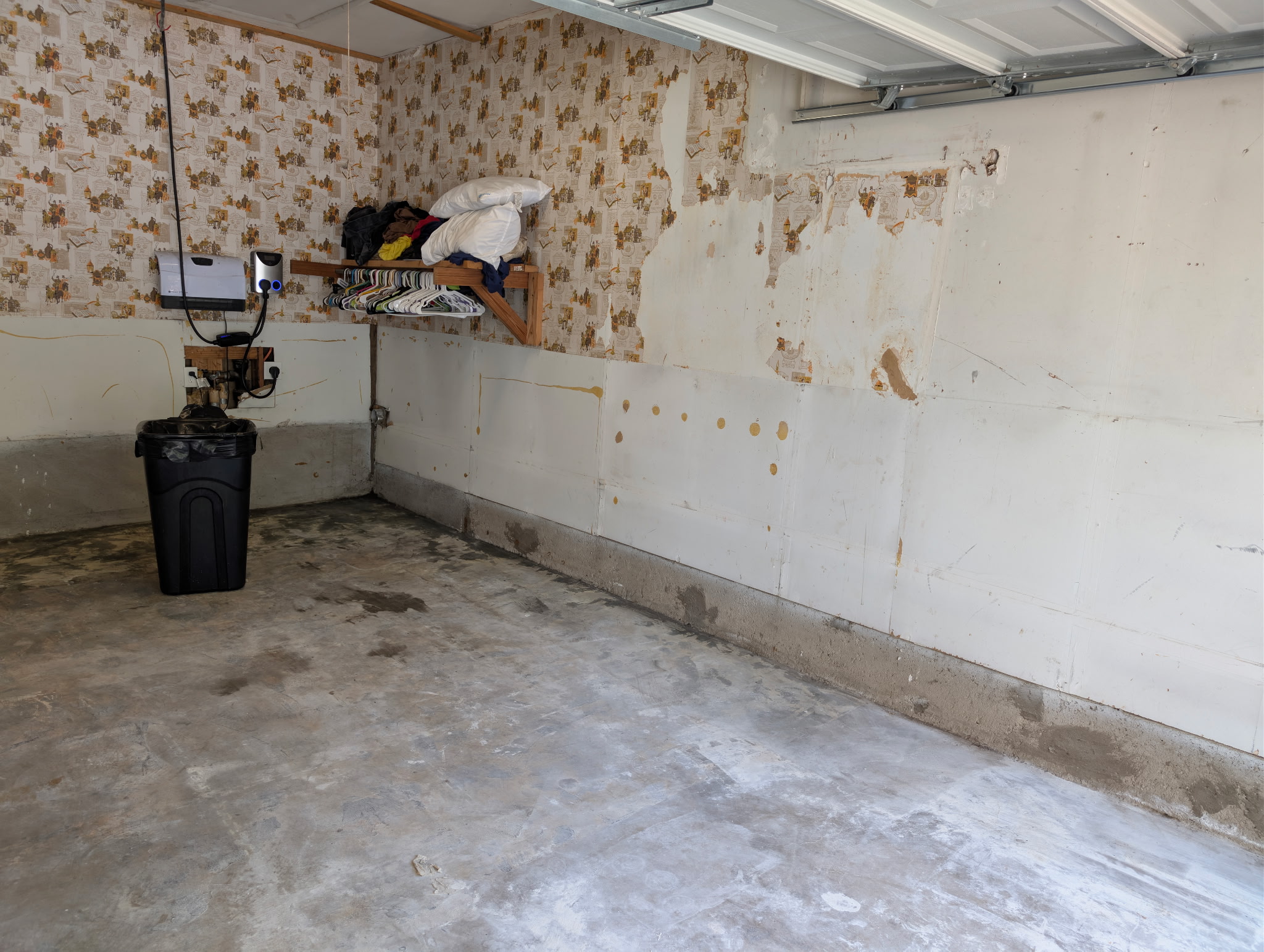 Empty single bay garage with gray uncoated concrete, a trash can and old wall paneling in Carrollton, TX